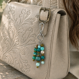 Beige handbag with a decorative purse charm featuring turquoise and gold beads.