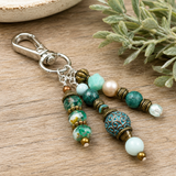 Beaded purse charm with decorative elements on a wooden surface with greenery