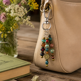 Beige handbag with a colorful beaded purse harm, book, and flowers on a wooden surface