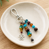 Colorful butterfly beaded hand bag charm with a silver clasp on a white ceramic dish.