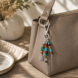 Beaded purse charm hanging from a beige handbag on a wooden surface with a plant in the background
