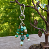 Beaded handbag charm with turquoise and gold beads on a branch with green foliage in the background