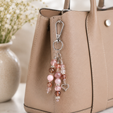 Beaded purse charm with heart charm attached to a beige handbag.