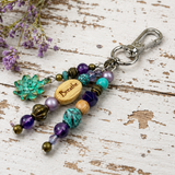 Colorful beaded yoga purse charm with 'Breathe' charm on a wooden surface with purple flowers.