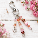 Beaded purse charm with a heart charm on a white wooden surface with pink flowers.