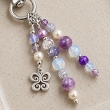 Purple Beaded purse charm with a butterfly charm on a beige background
