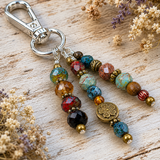 Colorful beaded purse charm with a metal clasp on a wooden surface with dried flowers.