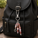Black backpack with a beaded bag charm featuring pink beads and a heart charm.