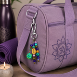Purple yoga bag with a lotus flower bag cham and yoga mat on a wooden surface